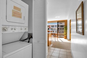A laundry area with a washing machine and dryer, a notice on the dryer, and a view of a balcony with a dining area and a building in the background.
