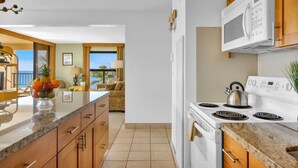 Una cocina moderna con una isla central, electrodomésticos blancos y vista a una sala de estar.