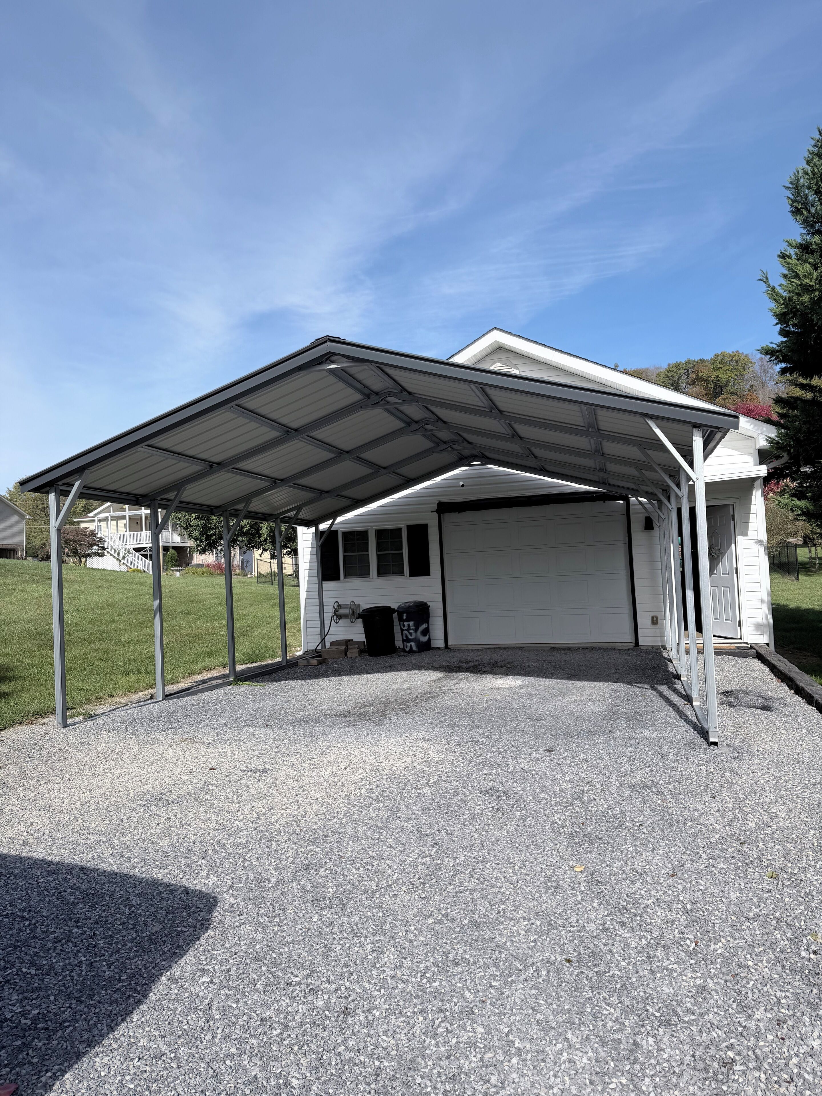 A covered garage with a gravel driveway and a metal roof structure.