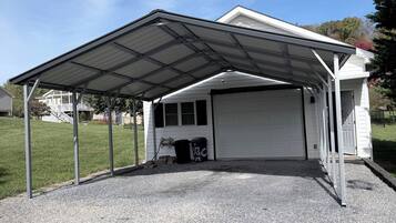 A covered garage with a gravel driveway and a metal roof structure.