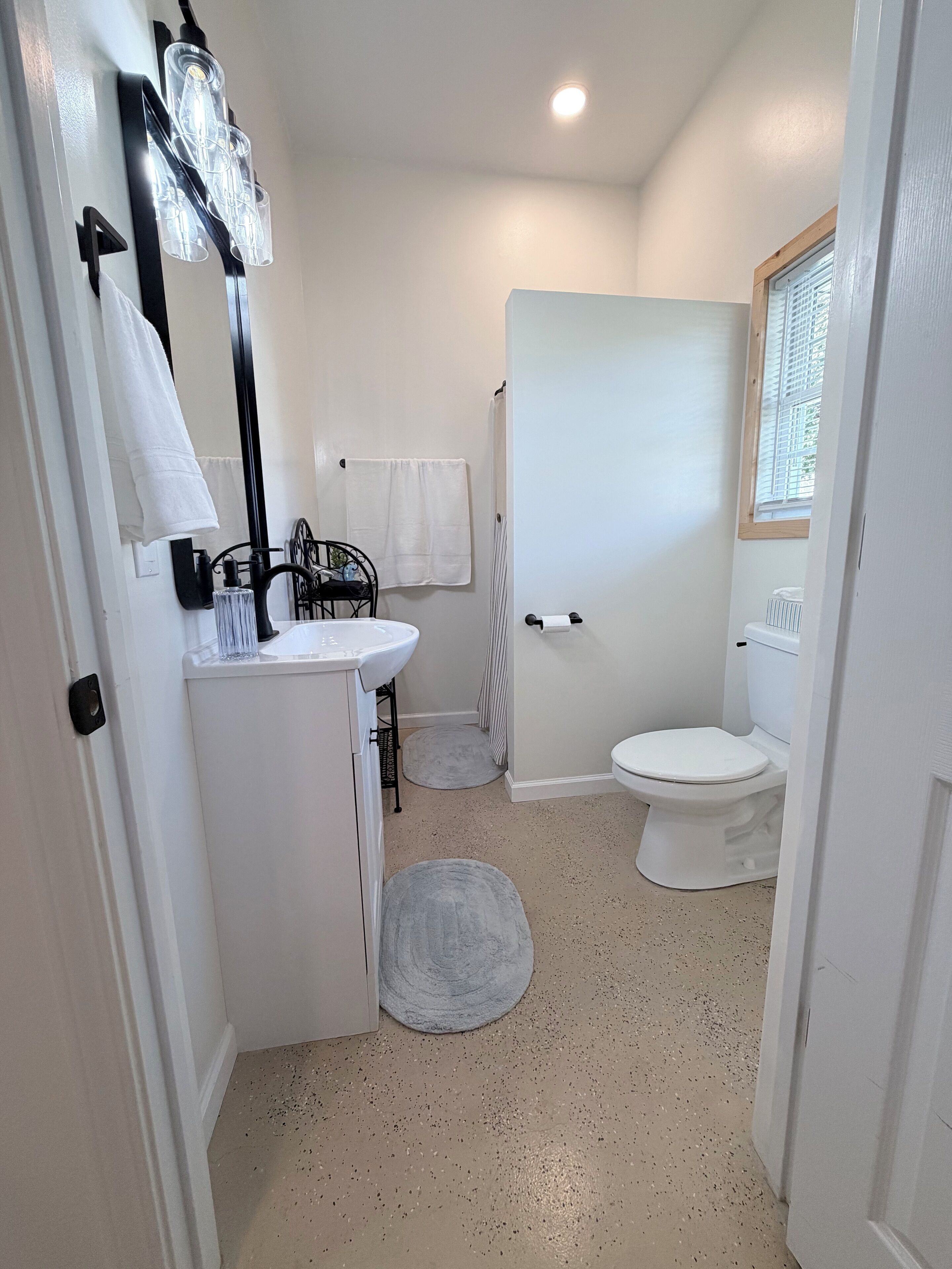 A compact bathroom with a white sink, black metal chair, and a toilet.
