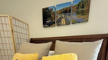 A bed with patterned bedding, three pillows, and two wall-mounted pictures depicting outdoor scenes.