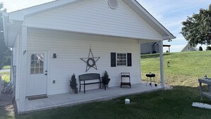 A white single-story building with a covered porch, a star decoration, a bench, and a small table. - Pet-Friendly Mountain Studio - Cozy Stay with Patio & Covered Private Parking (Kingsport)