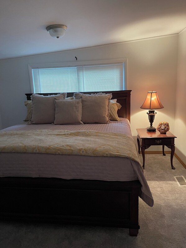 A bedroom with a large bed, a bedside table with a lamp, and a window with blinds.