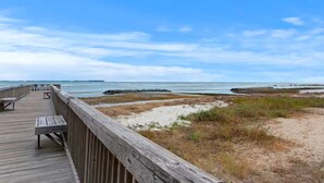 A wooden boardwalk leading to a beach with a clear view of the ocean and distant land.