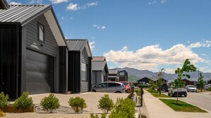 A row of modern, single-story houses with garage doors, parked cars, and a clear view of mountains in the background.