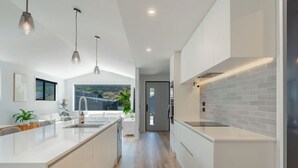 A modern kitchen with a central island, pendant lighting, and a view to the outdoors. - Executive 3BR 3Queen-Beds Free Unltd WiFi & Garage (Queenstown)