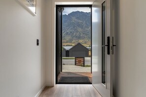 A modern interior with a sliding glass door leading to an outdoor area with a mountain view and a small building. - Executive 3BR 3Queen-Beds Free Unltd WiFi & Garage (Queenstown)