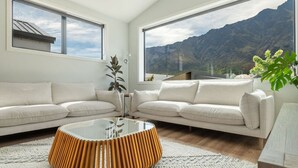 A modern living room with two white sofas, a glass coffee table, and a view of mountains through large windows. - Executive 3BR 3Queen-Beds Free Unltd WiFi & Garage (Queenstown)