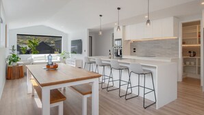 A modern kitchen with white cabinetry, a wooden dining table, and bar stools. - Executive 3BR 3Queen-Beds Free Unltd WiFi & Garage (Queenstown)
