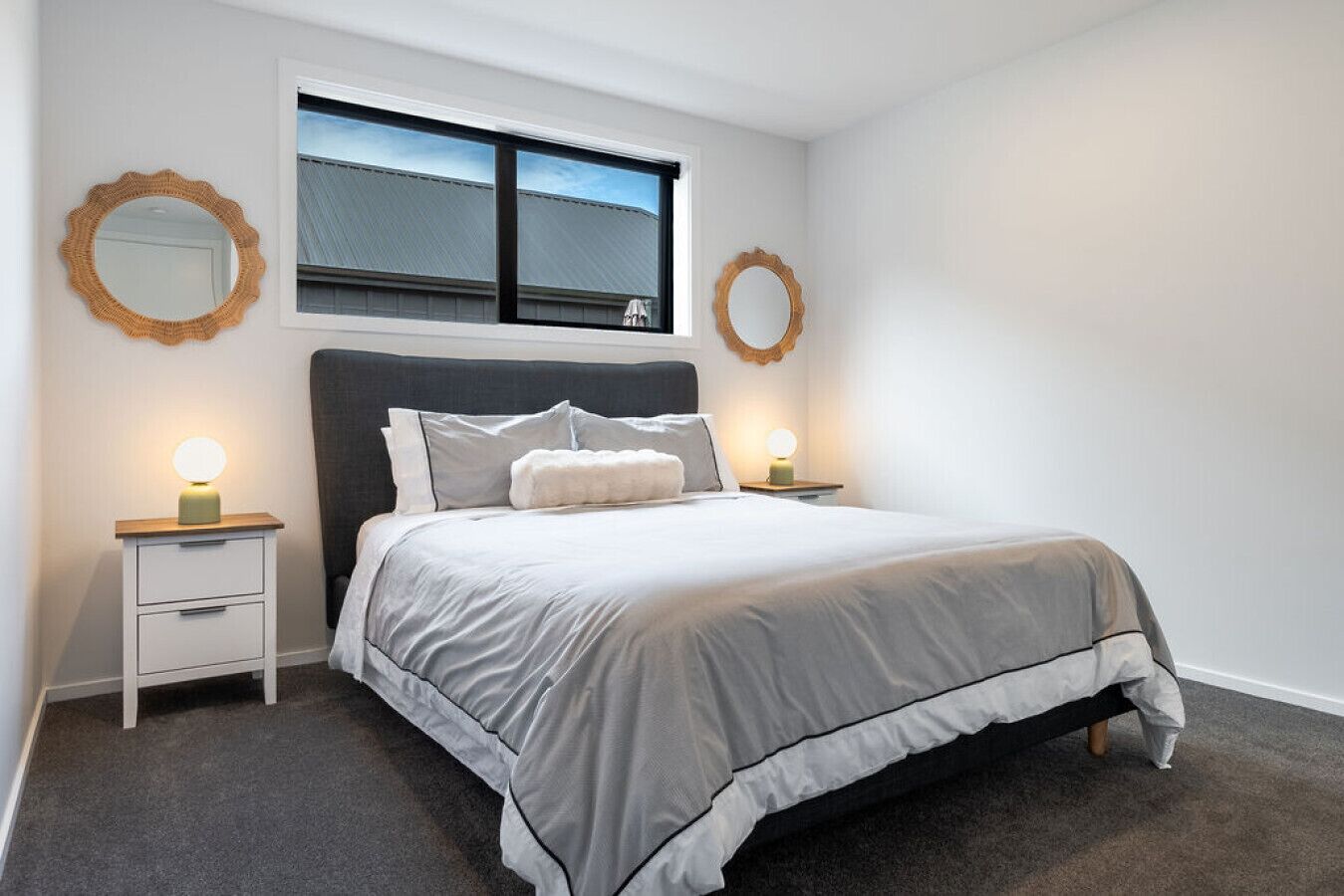 Een slaapkamer met een bed, twee nachtkastjes, twee spiegelwanden, een raam en uitzicht op een gebouw.