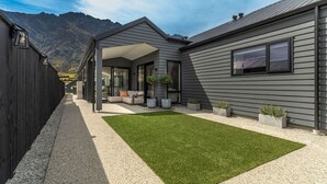 A modern house with a covered patio, a well-maintained lawn, and a mountain backdrop. - Executive 3BR 3Queen-Beds Free Unltd WiFi & Garage (Queenstown)
