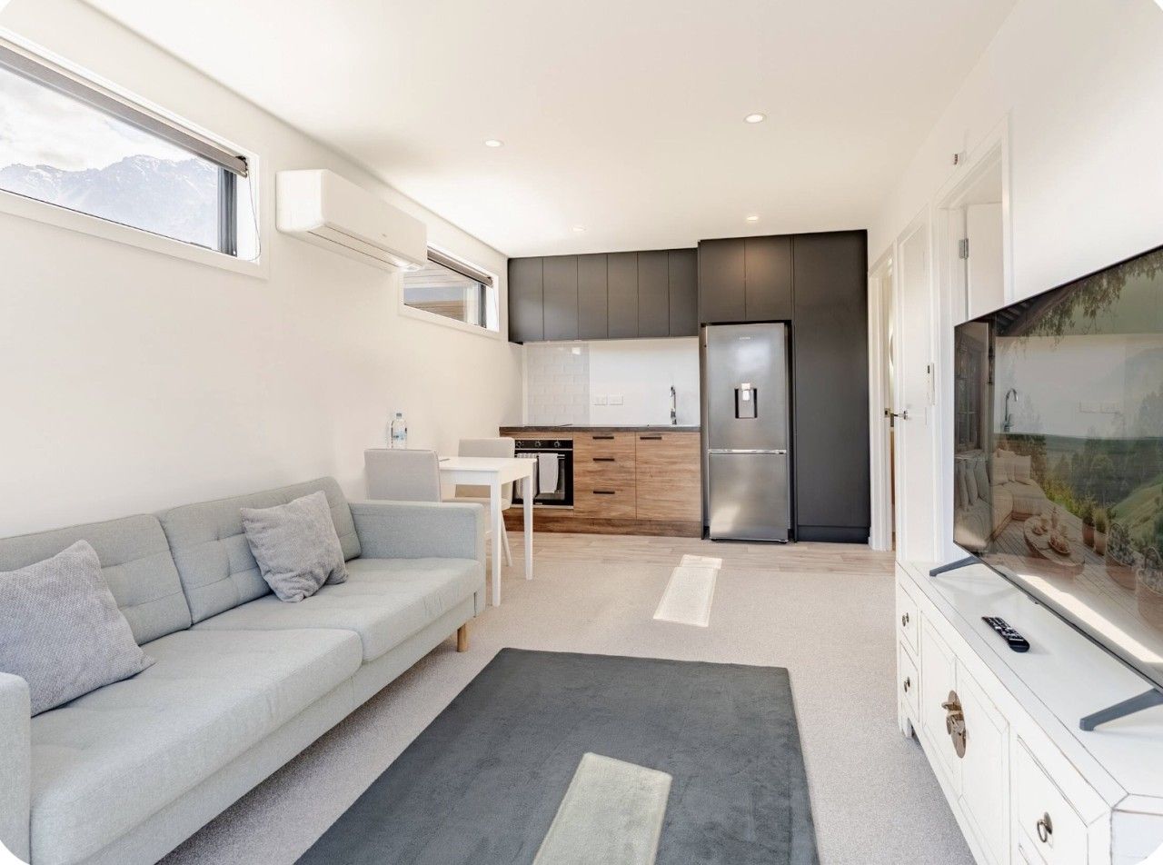 Un espacio habitable moderno con sofá, una mesa de comedor, una zona de cocina con refrigerador y un televisor sobre un mueble.