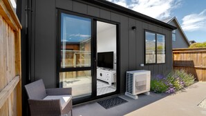 Una casa moderna con grandes puertas corredizas de vidrio, un patio con mobiliario de mimbre y un equipo de aire acondicionado.