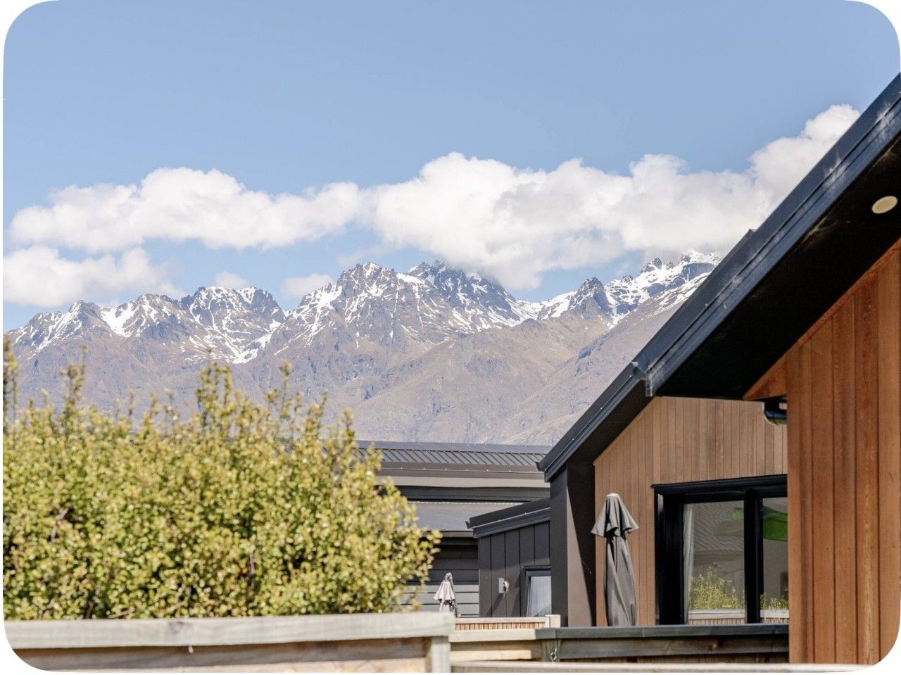 A modern building with a wooden exterior and large windows, set against a backdrop of snow-capped mountains.