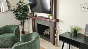 A living room with a fireplace, two green armchairs, a TV, and a small table with a plant. - Comfortable, Spacious home with pool table•firepit• great location (South Jordan)
