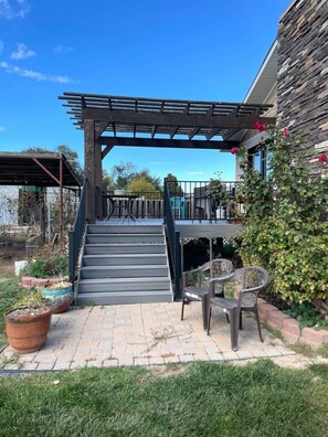Área externa coberta com pérgola, escadas para um varanda e um terraço com cadeiras.