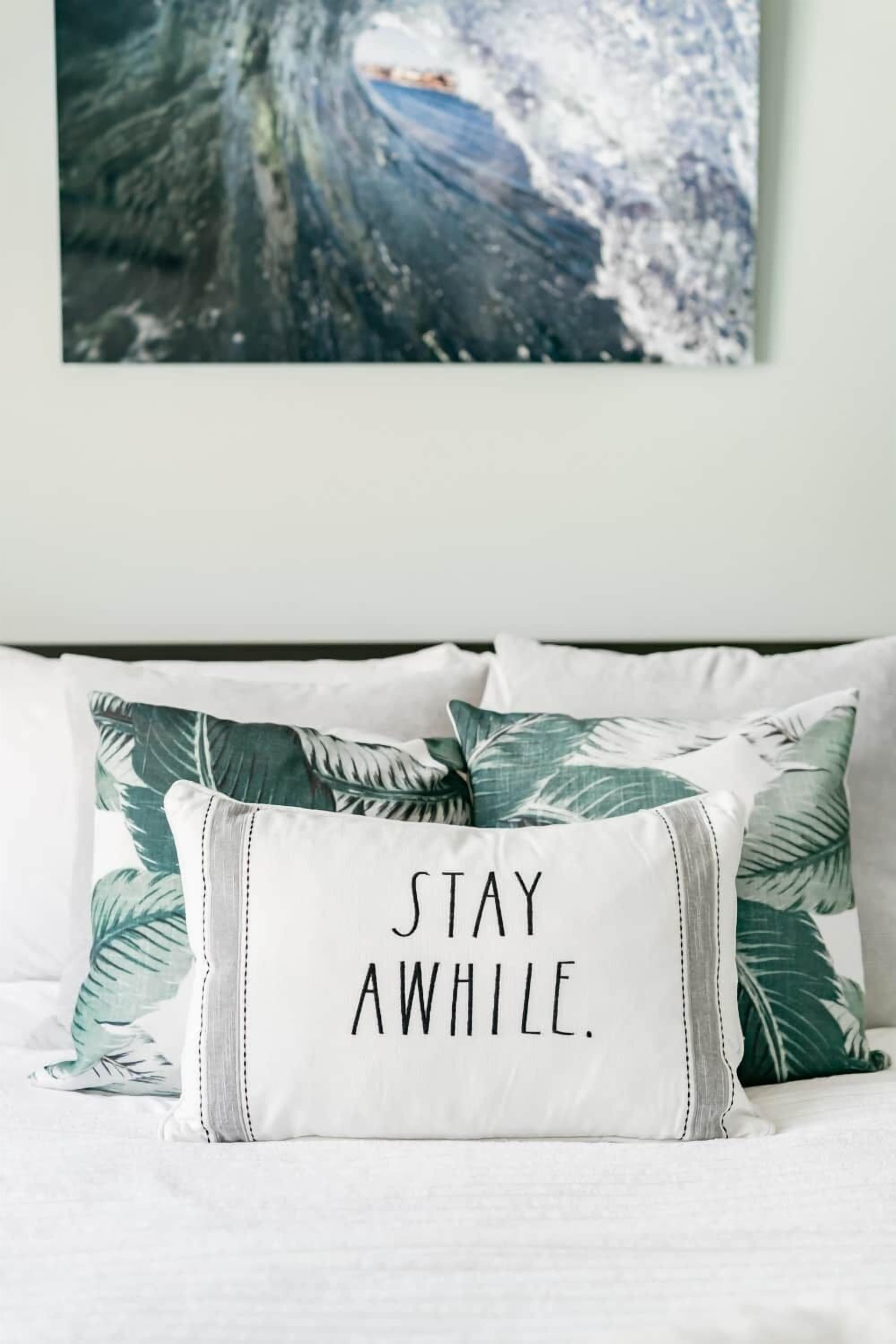 Una cama con un almohada que tiene el texto 'STAY AWAY' y otra almohada con un diseño de hojas tropicales.