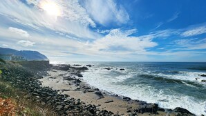 Une plage rocheuse avec des vagues, un ciel dégagé et une maison qui se profile à l’horizon.