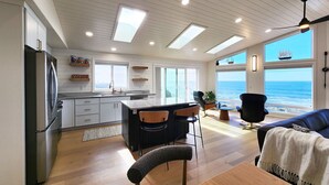 Une cuisine moderne dotée d’un îlot central, un coin repas offrant une vue sur l’océan et un espace salon confortable avec vue sur la mer.