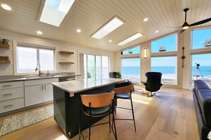 A modern kitchen with a large island, bar stools, and a view of the ocean. - Beautiful Ocean Views! Walk to Everything! Mermaid's Perch (Yachats)