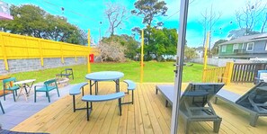 Une terrasse extérieure avec une table et des chaises, entourée d’une clôture en bois et de verdure.