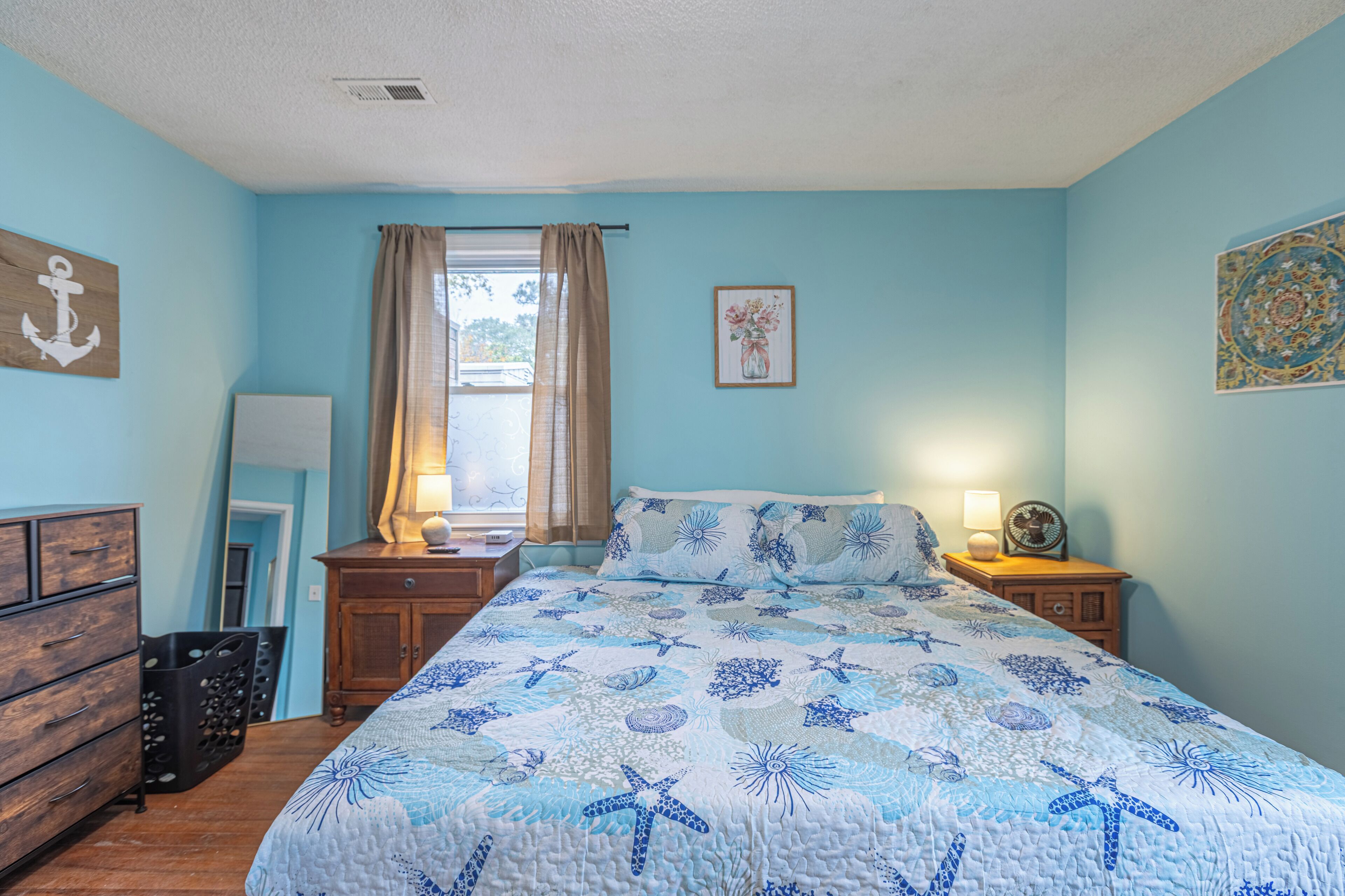 A bedroom with a bed, wooden nightstands, a dresser, and a window with curtains.