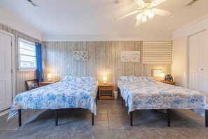 Une chambre avec deux lits, des murs recouverts de panneaux en bois et un ventilateur de plafond.