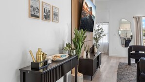 A modern living room with a black console table, a TV mounted on the wall, and a dining area with a black chair and a mirror. - Luxury home Minutes to Armature works & Downtown! (Tampa)