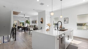 A modern kitchen with a central island, a dining area with a sofa and chairs, and a ceiling fan. - Luxury home Minutes to Armature works & Downtown! (Tampa)
