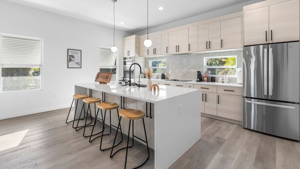 A modern kitchen with a central island, bar stools, stainless steel appliances, and light wood cabinetry. - Luxury home Minutes to Armature works & Downtown! (Tampa)