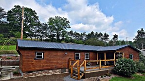 A wooden cabin with a metal roof, a porch, and a small garden area. - Newly Renovated Home in Huntingdon- Near Juniata, Penn State, & Raystown Lake (Huntingdon)