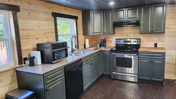 A modern kitchen with wooden walls, stainless steel appliances, and a window providing natural light. - Newly Renovated Home in Huntingdon- Near Juniata, Penn State, & Raystown Lake (Huntingdon)