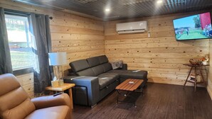 A cozy cabin interior with a leather sofa, a wooden table, and a television mounted on the wall. - Newly Renovated Home in Huntingdon- Near Juniata, Penn State, & Raystown Lake (Huntingdon)