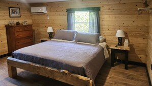 A wooden-paneled bedroom with a bed, two bedside tables with lamps, a dresser, and a window with curtains. - Newly Renovated Home in Huntingdon- Near Juniata, Penn State, & Raystown Lake (Huntingdon)