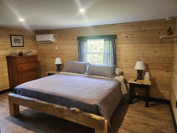 A wooden-paneled bedroom with a bed, two bedside tables with lamps, a dresser, and a window with curtains.