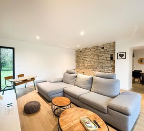 Una sala de estar moderna con un sofá seccional gris, una mesa de centro redonda de madera y una pared de piedra.