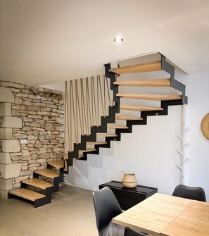 Un interior moderno con una pared de piedra, una escalera de madera y un comedor con mesa y sillas.