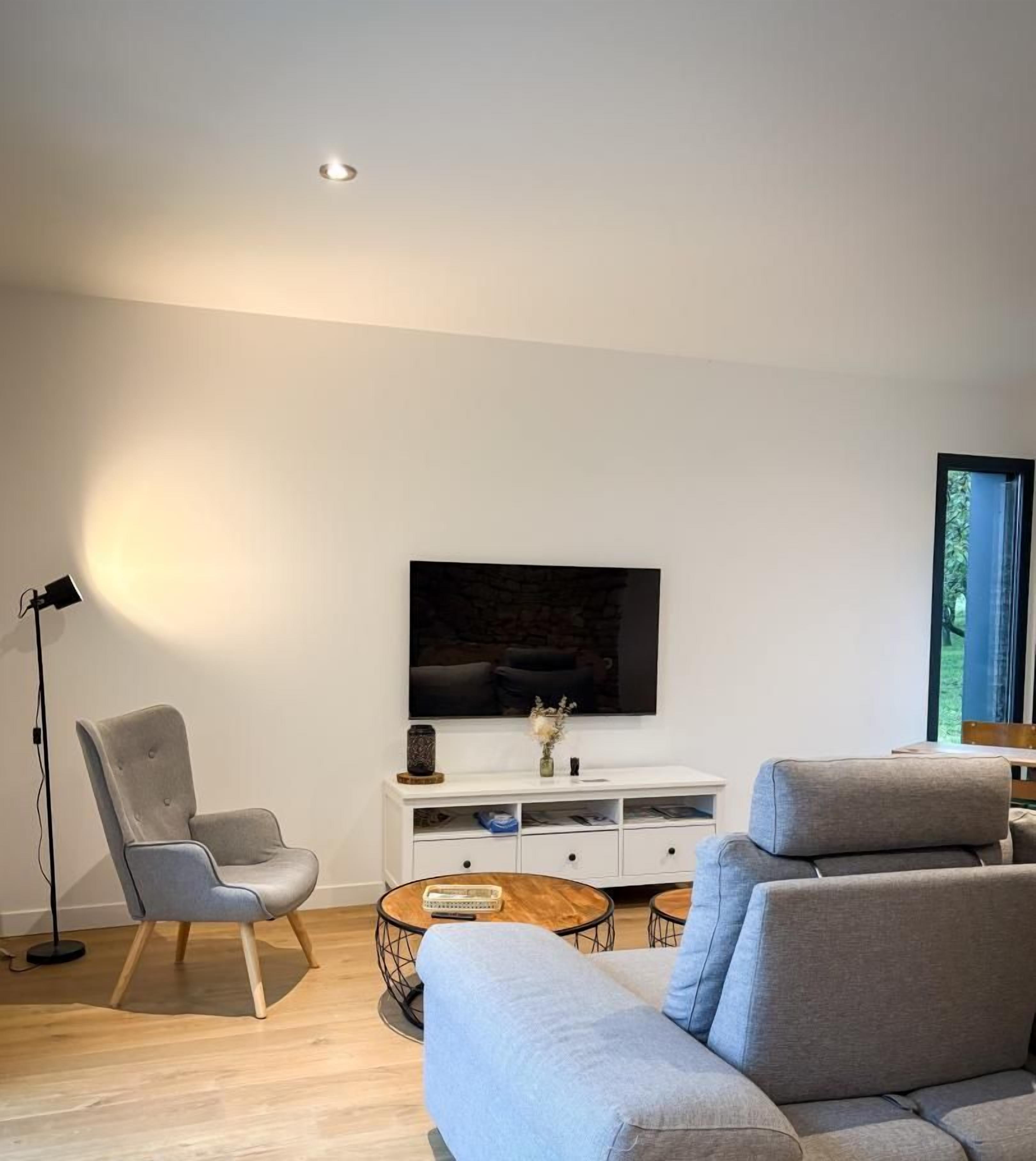 Uma sala de estar moderna com um sofá cinzento, uma poltrona, uma mesa de centro e uma TV de tela plana sobreposta a um armário branco.