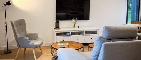 A modern living room with a grey sofa, a chair, a coffee table, and a flat-screen TV on a white cabinet.