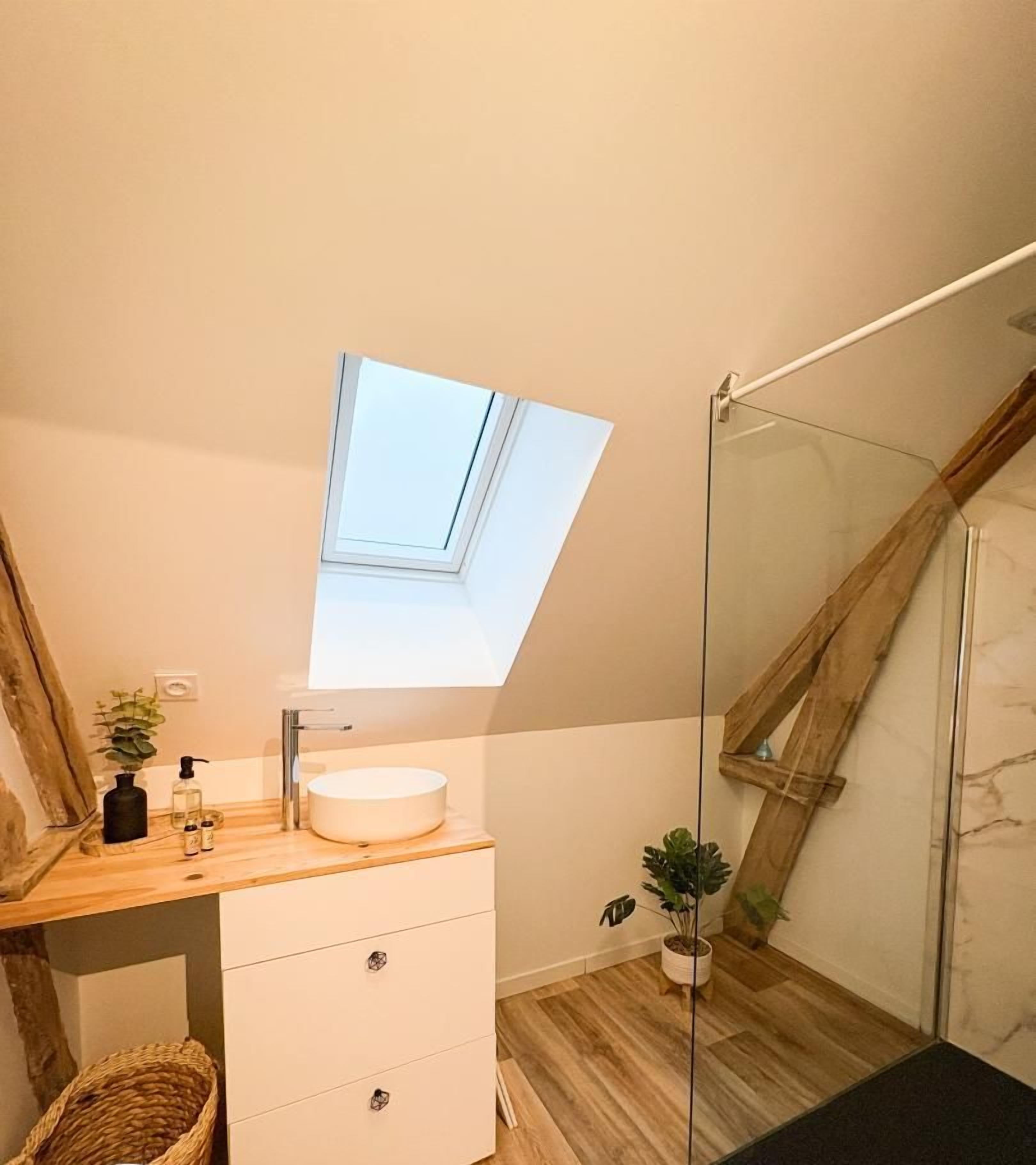 Une salle de bain moderne dotée d’un puits de lumière, d’un meuble-lavabo en bois et d’une cabine de douche en verre.