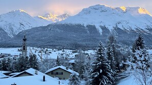 Un village enneigé, avec un clocher d’église et des montagnes en arrière-plan.