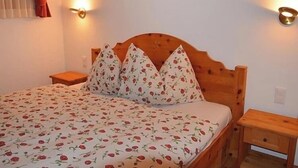 Une chambre à coucher avec une tête de lit en bois, une literie à motifs floraux, deux tables de chevet et des lampes fixées au mur.