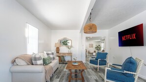 A modern living room with a sofa, coffee table, and armchair, a television mounted on the wall, and a hanging light fixture. - House in North Rose, NY, 10 minutes from the beach (North rose)
