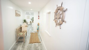 A hallway with a wooden bench, a surfboard, and a ship's wheel decoration on the wall. - House in North Rose, NY, 10 minutes from the beach (North rose)