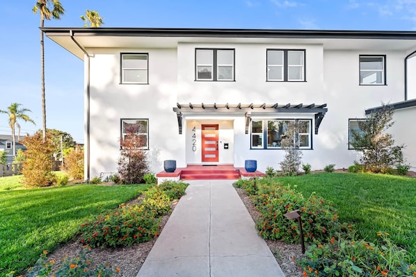A modern two-story house with a red door, a front porch, and a well-maintained lawn.
