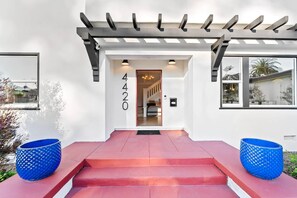A modern house with a red entrance, a number '4420' on the wall, and a covered porch with a pergola.