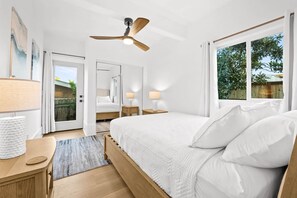 A bedroom with a bed, bedside tables, a ceiling fan, and a view of the outdoors.