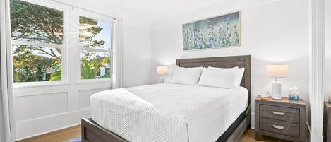 A bedroom with a bed, a nightstand, a lamp, a ceiling fan, and a window with a view of trees.