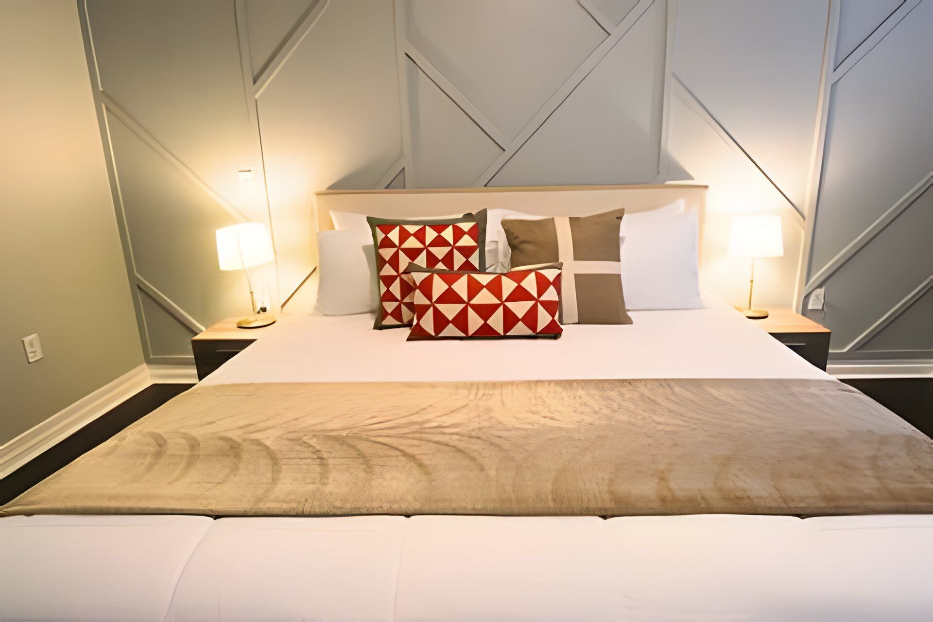Une chambre d’hôtel avec un grand lit, deux lampes de chevet et une tête de lit ornée d’un motif géométrique.